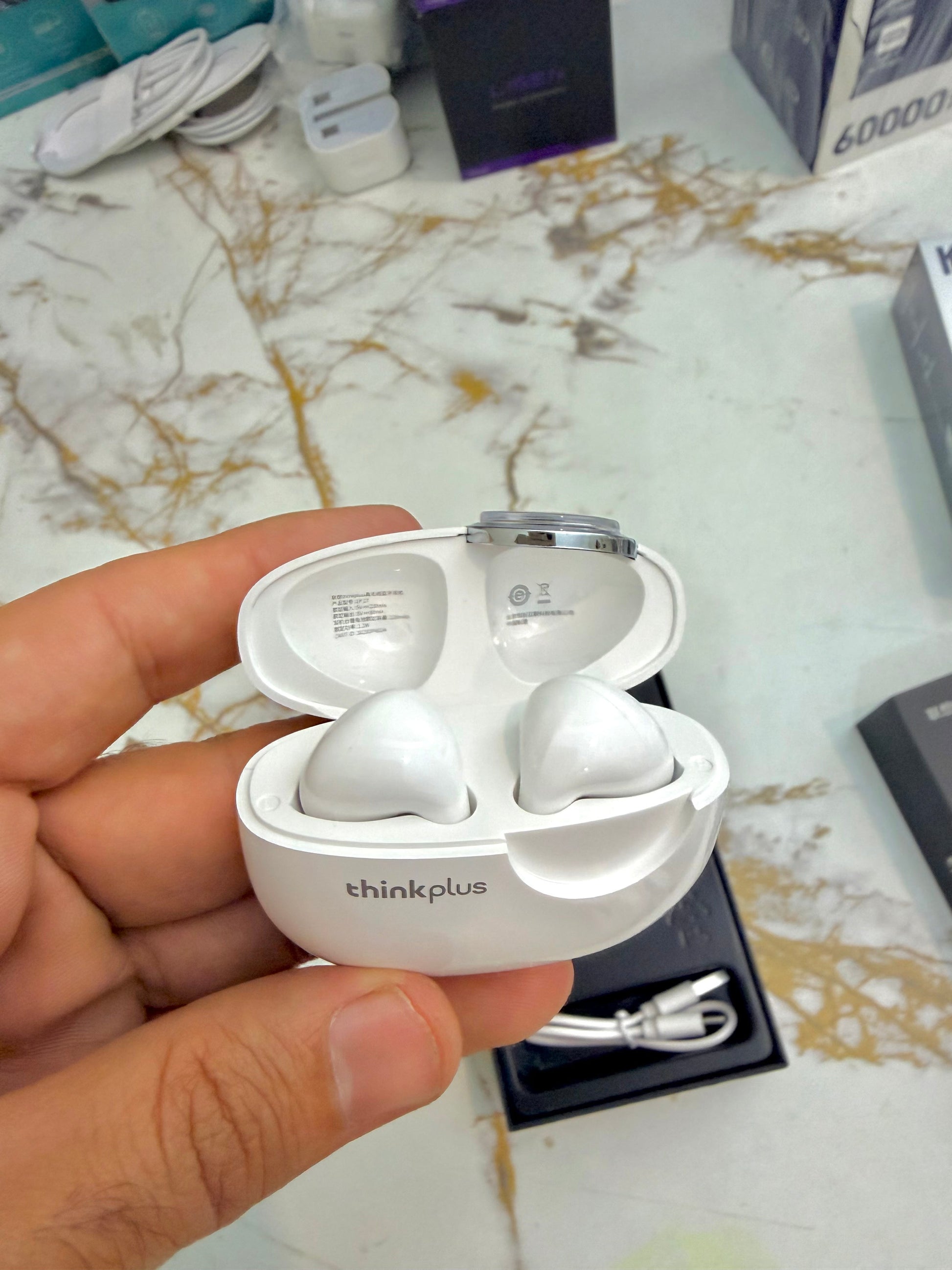 White earbuds with charging case held by a hand on a marble surface