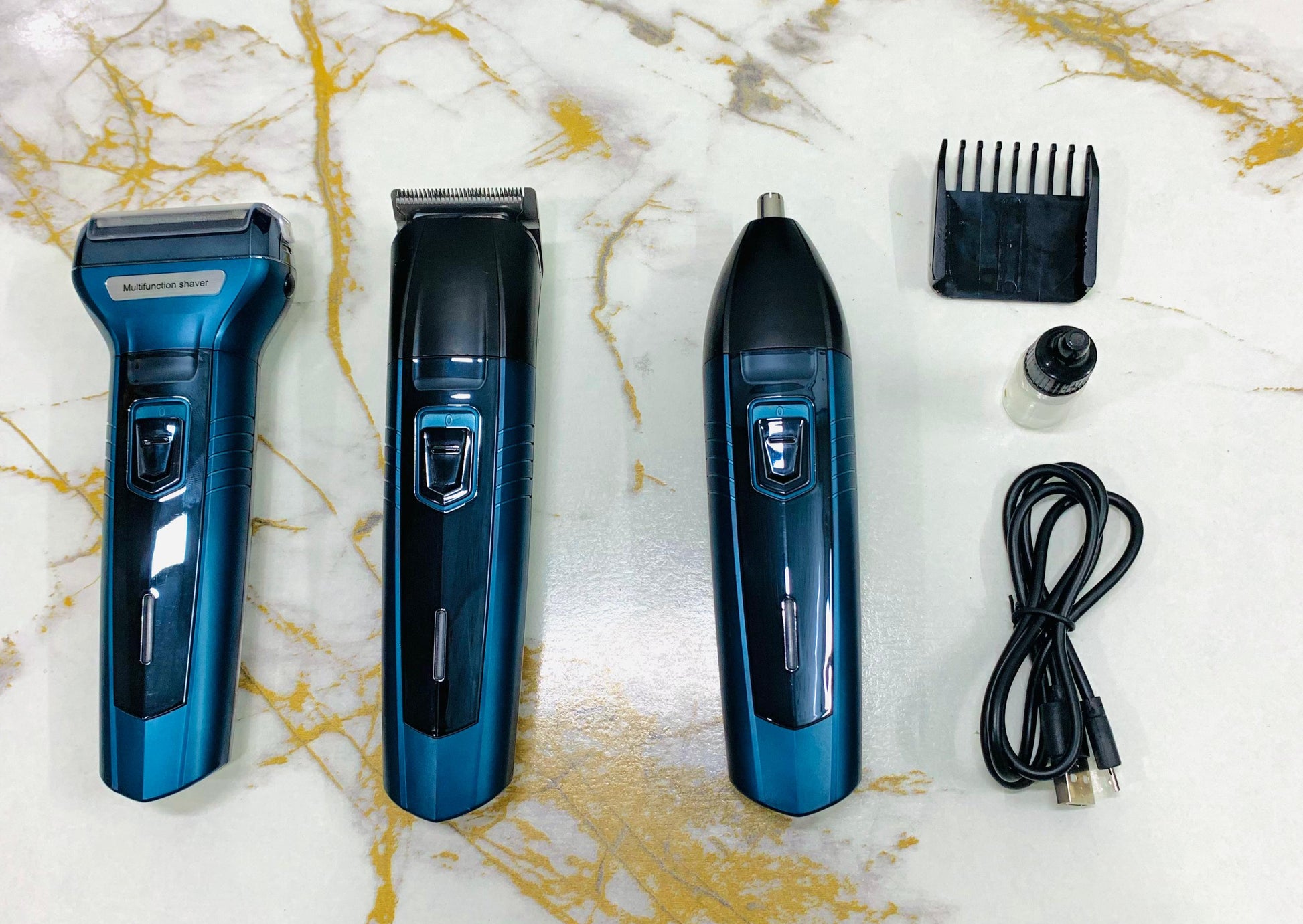 Set of grooming tools including a shaver, trimmer, and hair dryer on a marble surface.